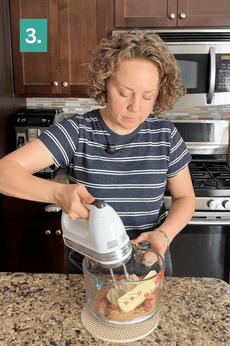 A person mixes ingredients with a hand mixer in a glass bowl on a kitchen counter. A green box with the number 3 appears in the top left corner.